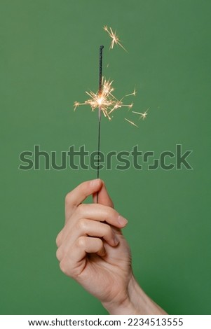 Bengal fire burning on green isolated background, vertical image. Female hand holding sparklers. Concept of winter holidays Royalty-Free Stock Photo #2234513555
