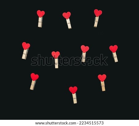 On a black background, small clothespins with red hearts are randomly laid out. There are many miniature clothespins with hearts lying nearby. Concept of valentine's day or love relationship