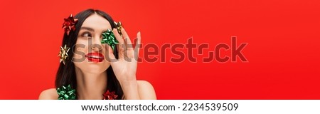 Model with visage and gift bows on hair looking away isolated on red, banner