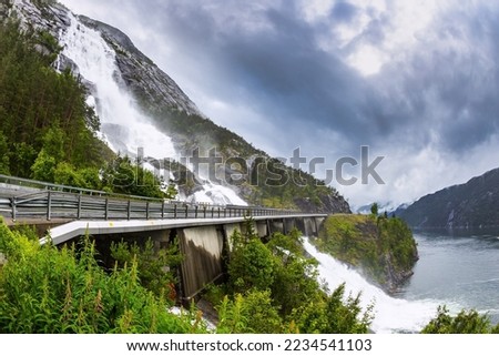 The cascading powerful Langfossen waterfall intersects with the highway and flows into the Acre Fjord. Western Norway. Majestic natural phenomenon. Unique wonder of nature