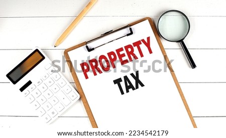 PROPERTY TAX words on a clipboard, with calculator, magnifier and pencil on the white wooden background