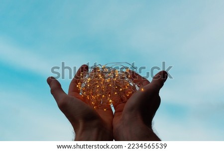 Lights in male hands. Garland on the backdrop of the blue sky. Christmas and New Year lights concept. Hands holding glowing lamps. Romantic background. Hope and faith.