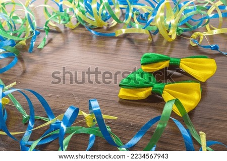 Bow tie with brazil colors on a wooden table with green, yellow and blue ribbons.