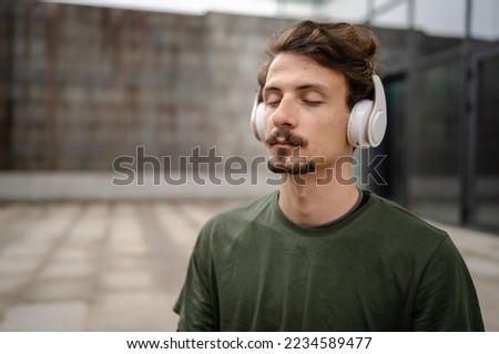 One man young adult caucasian male eyes closed for guided training yoga or meditation while sitting outdoor with headphones self-care practice real people well-being inner peace and balance concept Royalty-Free Stock Photo #2234589477