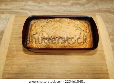 A freshly baked apple bread in a stone loaf mold on top of a wooden cutting board cooling off.