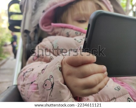A little girl looks into a mobile phone. The child is addicted to watching content.