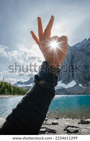 The young wanderer high in the mountains captures the sunset over Floe Lake,East Kootenay, British Columbia,Canada . Ideal timing capturing rays shining from his hand. Royalty-Free Stock Photo #2234611299