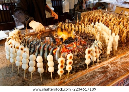 Around a charcoal fire, a stall vendor roasting skewered Iwana fish and Kushi Dango, which is made from rice flour and a street-food popular with Japanese people (in Yumoto, Oku-Nikko, Tochigi, Japan)