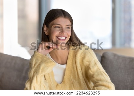 Joyful pretty young woman indoor candid portrait. Beautiful girl with healthy white teeth smiling, looking away, touching chin, thinking, dreaming, promoting beauty care, dentistry, healthcare