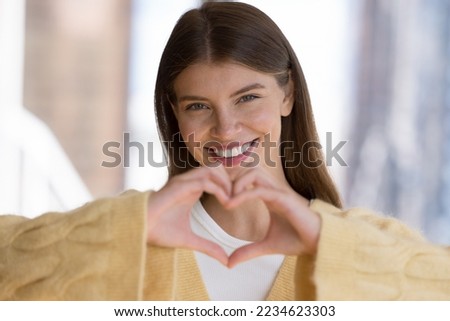 Happy carefree pretty girl in casual showing finger heart shape, symbol of love, romance, happiness. Blogger, influencer woman girl sharing emotions, making hand like gesture, smiling at camera