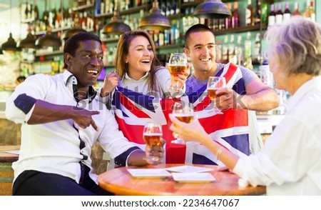 Emotional male and female drinking beer and celebrating success of sports team, waving flag of the Great Britain, man showing victory sign at bar