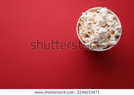 Paper bucket with delicious popcorn on red background, top view. Space for text
