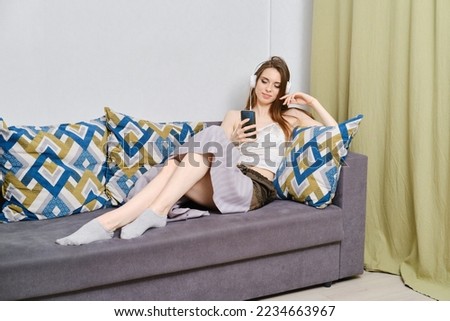 Music therapy. Full-length of young and calm woman in headphones lying under rug on comfortable couch at home, listening to favorite radio station or musician and smiling happily