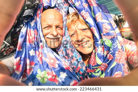 Senior happy couple taking a selfie at the week clothes market traveling around the world - Concept of active elderly and interaction with new technologies and trends - Bright vintage filtered mood