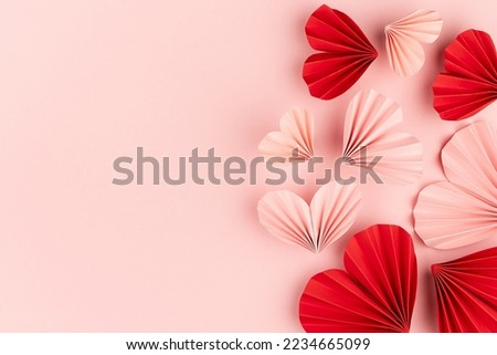 Tender pink and passion red hearts of chinese paper fans flying on pastel pink color as romantic Valentine day background, sideways border, top view, copy space, closeup.