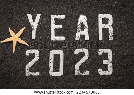 Happy New Year 2023 concept with a shell and a starfish on black beach sand. Winter vacations in the sun.