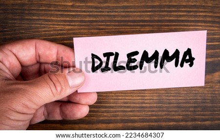 DILEMMA. Pink piece of paper with text in man's hand on wood texture background.