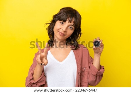 Young latin woman holding compass isolated on yellow background smiling and showing victory sign