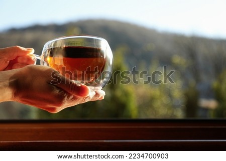 Female hands hold cup of hot drink near windowsill Royalty-Free Stock Photo #2234700903