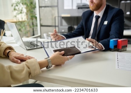 Close up of unrecognizable woman applying for visa in US immigration office and handing documents Royalty-Free Stock Photo #2234701633