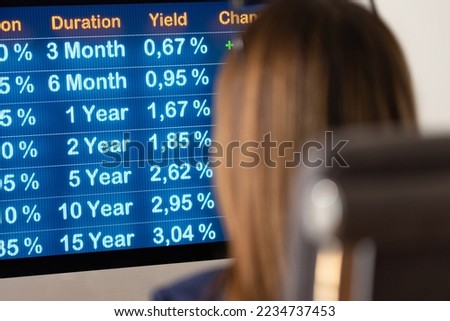Businesswoman siting at the desk and looks the current interest rates on the Screen. Close-up computer monitor with rising yields. Financial business, mortgage rates, debt financing and loan.