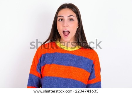 Oh my God. Surprised Young caucasian woman wearing colorful sweater over white background stares at camera with shocked expression exclaims with unexpectedness,