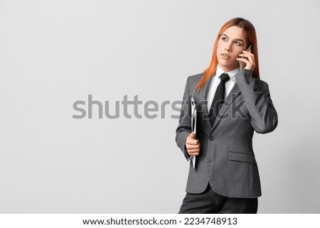 Beautiful transgender secretary with clipboard talking by mobile phone on grey background