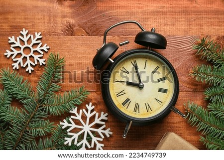 Alarm clock with Christmas branches and snowflakes on wooden background
