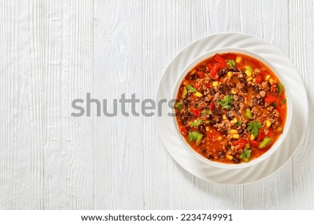 taco soup of ground beef, tomatoes, chopped green chilis, onions, corn, red beans and taco seasoning in white bowl, horizontal view from above, flat lay, free space