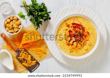 savory creamy pumpkin soup topped with fried bacon, shredded cheddar cheese and salty croutons in white bowl on wood table with ingredients, horizontal view from above, flat lay Royalty-Free Stock Photo #2234749993