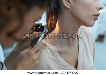 Dermatologist in latex gloves holding dermatoscope while examining attractive patient with skin disease. Female dermatologist examining patient with dermascope, looking for signs of skin cancer.