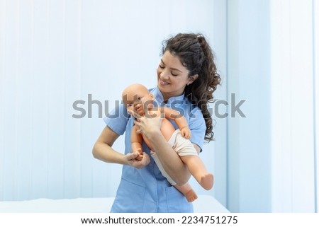 CPR practitioner examining airway passages on infant dummy. Model dummy lays on table and two doctors practice first aid. Royalty-Free Stock Photo #2234751275