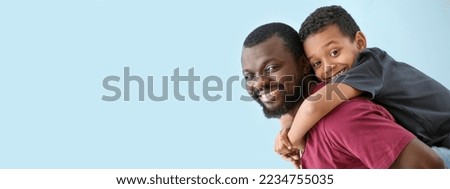 Portrait of happy African-American man and his little son on light blue background with space for text