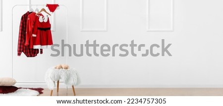 Hanger with Christmas clothes and Santa hat near white wall in room