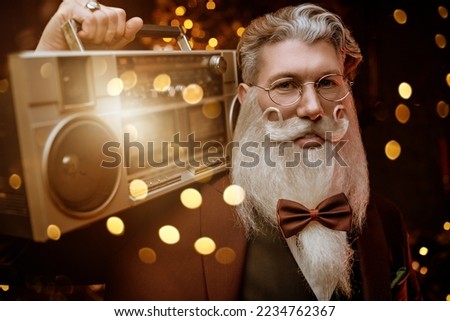 Portrait of a handsome Santa Claus in an elegant three piece suit holding a tape recorder in his hands in a magical Christmas light. Fun fashionable party for Christmas and New Year.