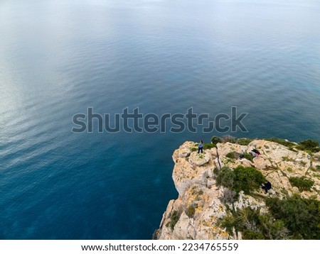 Person standing on a cliff looking towards the horizon, Aerial views with drone in the european coast, balearic islands. View of the same cliff and the sea at his feet.