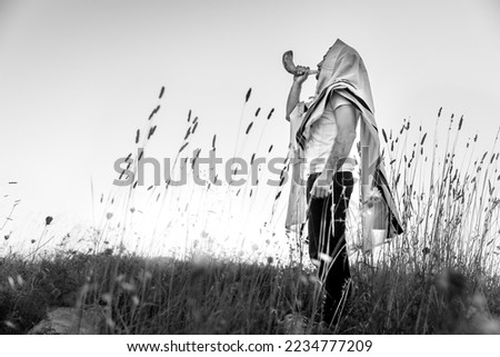 Jewish man in a traditional tallit prayer shawl blowing the ram's horn shofar on Rosh HaShana and Yom kippur .black and white photography Royalty-Free Stock Photo #2234777209