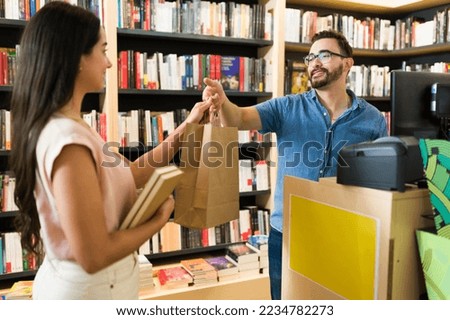 Caucasian happy worker giving the shopping bag to a customer reader buying books at the bookstore Royalty-Free Stock Photo #2234782273