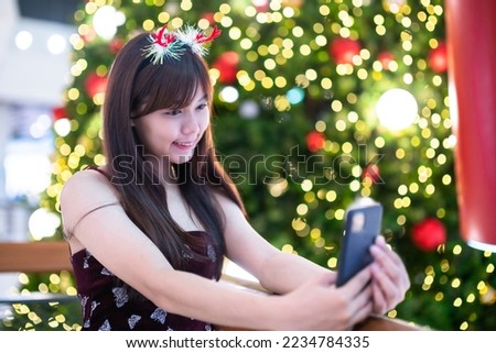 Portrait young asian woman red dress costume Take a selfie with a smartphone and picture parcel decoration on Christmas tree light circular bokeh background Decoration During Christmas and New Year.