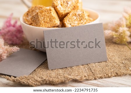 Gray business card with traditional turkish delight (rahat lokum) in white ceramic bowl on a white wooden background. side view, close up.