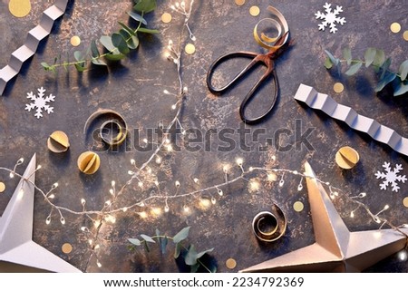 Handmade DIY Christmas or New Year decorations from cardboard. Top view, flat lay with lights on Xmas garland, golden paper balls, snowflakes, eucalyptus. Merry Christmas, Happy New Year background.