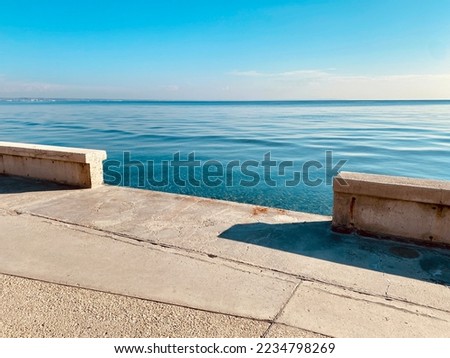 Long empty concrete promenade stree along the blue mediterranean sea under clouded sky
