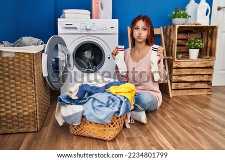 Young caucasian woman doing laundry holding socks puffing cheeks with funny face. mouth inflated with air, catching air.  Royalty-Free Stock Photo #2234801799
