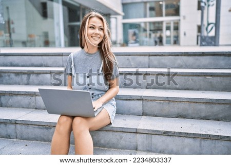 Young caucasian girl smiling happy using laptop sitting on the stairs at the city.