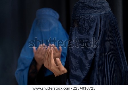 Two Arab female Muslim in Burka or Burqa traditional clothes  in Afghanistan and West Pakistan, praying Dua open hands to Allah, on dark background