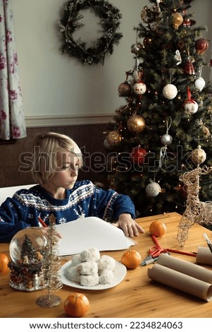 Concentrated boy writing letter to Santa Claus with Christmas tree at background