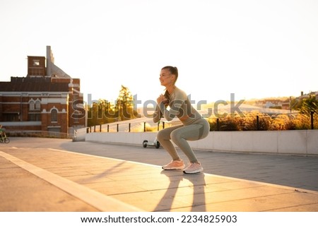 Sporty woman doing jumping squats exercises on stairs in park. Bodyweight training on sunset. Young adult fitness woman exercising outdoor. European woman squats. Athletic caucasian female workout Royalty-Free Stock Photo #2234825903