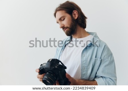 Man hipster photographer in a studio on a white background looking at the camera screen and setting it up for a photo shoot