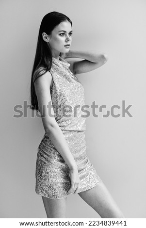 Black and white photo of a woman in a stylish sequined party dress posing near a wall