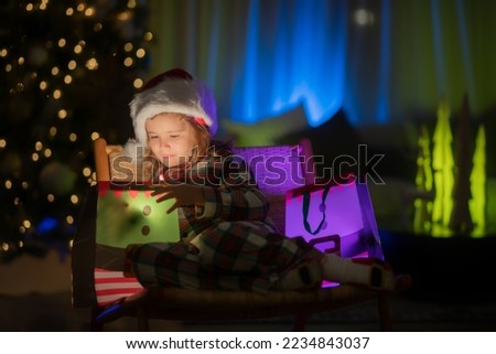 Kid with present gift with magic light. Lighting present gift bag. Kid in Christmas pajama enjoying winter holiday evening at home near the night Christmas tree.